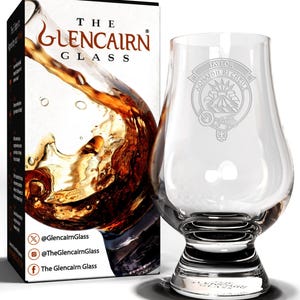 May include: A clear glass Glencairn whisky glass with a traditional design. The glass is engraved with the text "TAYLOR MONAIBH RI CHEILE" and a crest. The glass is sitting on a white surface.