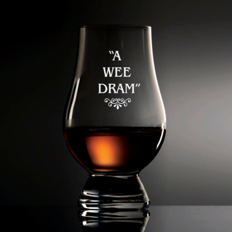 Puede incluir: Una copa de degustaci&oacute;n de whisky transparente con las palabras "A WEE DRAM" en letras blancas. La copa est&aacute; parcialmente llena de l&iacute;quido color &aacute;mbar. La copa tiene un cuerpo bulboso y un borde acampanado, con un tallo corto y una base ancha.