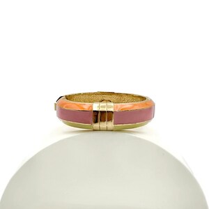 May include: A gold ring with a pink and orange enamel band. The ring is sitting on a white display stand.