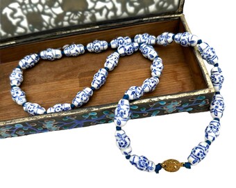 May include: A white and blue porcelain bead necklace with a gold clasp. The necklace is in a wooden box with a floral design.