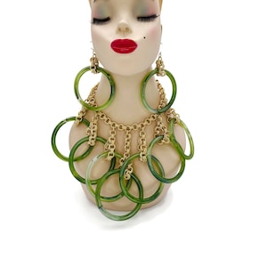 May include: A gold chain necklace with green plastic rings. The necklace is layered with multiple rings of different sizes. The necklace is displayed on a mannequin.