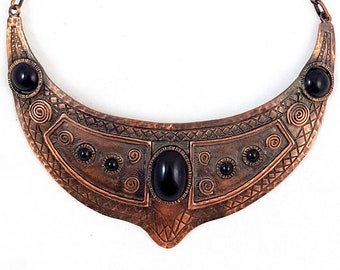 Puede incluir: Un collar de cobre con un colgante en forma de media luna adornado con piedras negras y diseños intrincados.