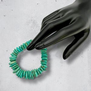 May include: A turquoise gemstone bracelet made of round, flat beads. The bracelet is on a white background.