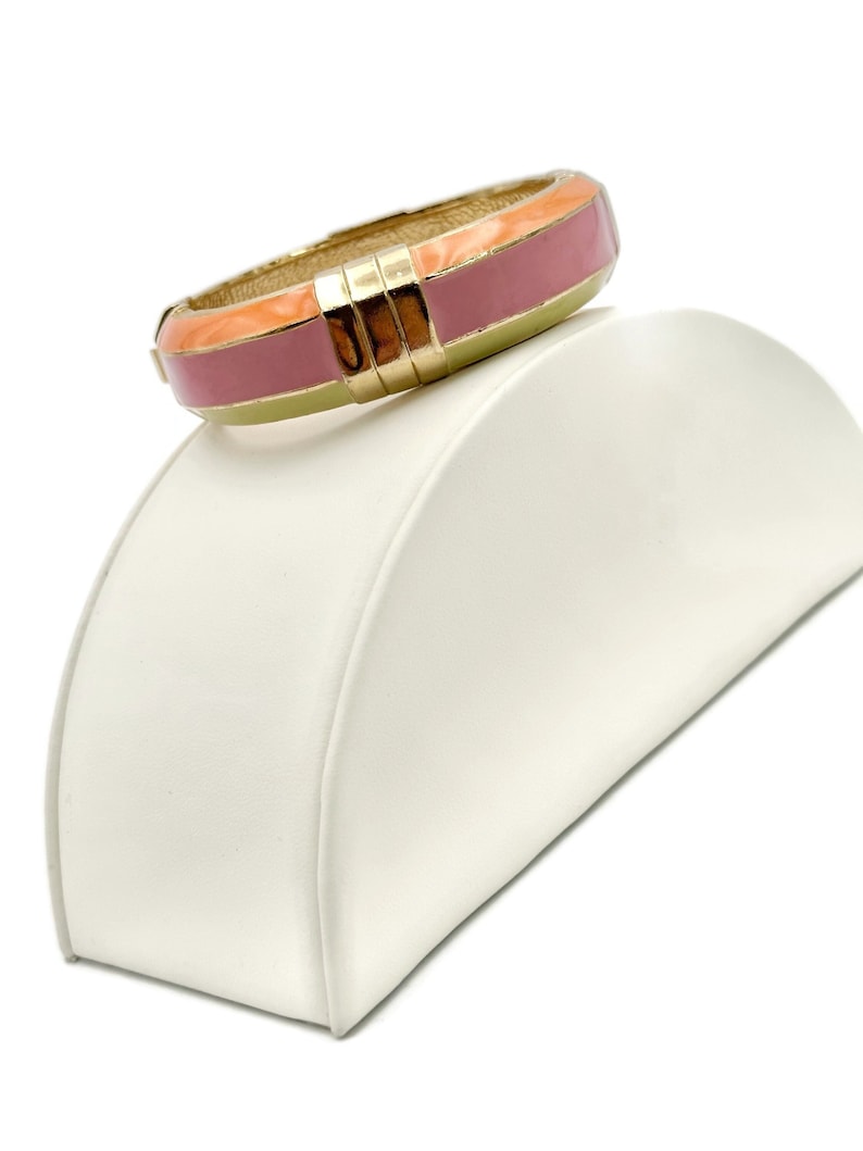 May include: A gold bangle bracelet with a pink, orange, and yellow enamel design.