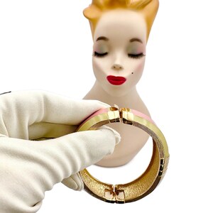 May include: A gold and pink hinged bangle bracelet. The bracelet is made of metal and has a smooth, polished finish.