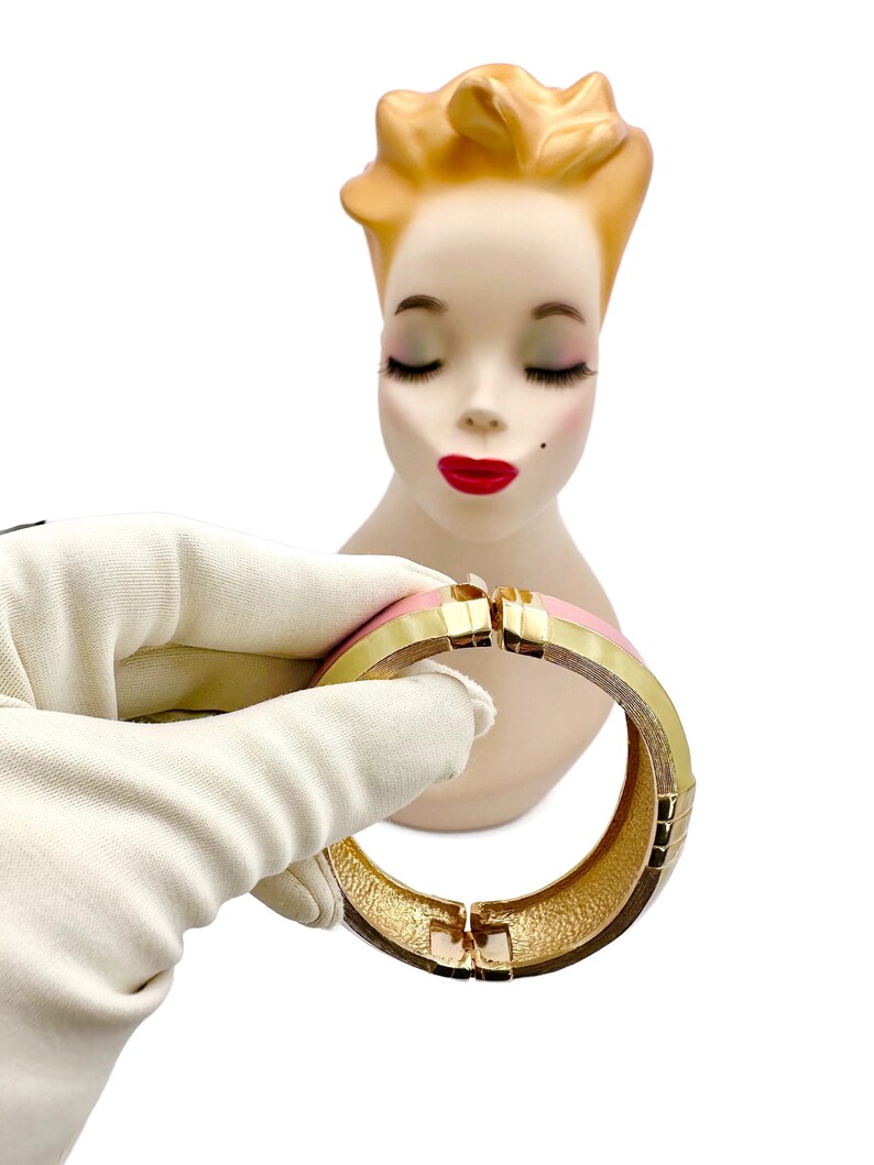 May include: A gold and pink hinged bangle bracelet. The bracelet is made of metal and has a smooth, polished finish.