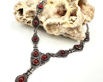 May include: A silver necklace with a pendant and red carnelian stones. The necklace is on a white rock background.