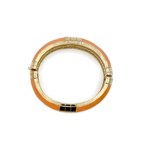 May include: A gold and orange bangle bracelet with a geometric design.