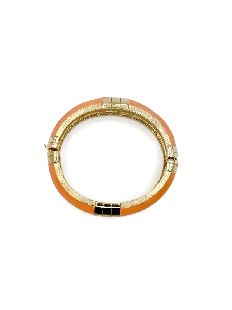 May include: A gold and orange bangle bracelet with a geometric design.