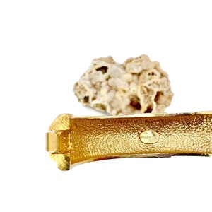 May include: Gold-toned metal bracelet with a textured surface and a circular logo that reads "VALENTINO" on the inside.