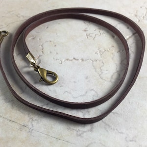Peut inclure: Un collier en cordon de cuir marron avec un fermoir en laiton.