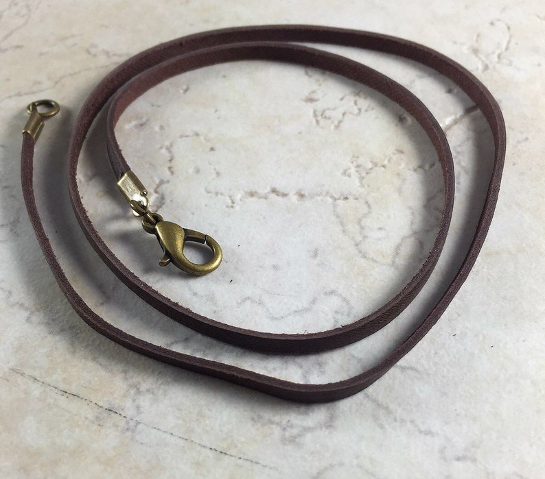 Peut inclure: Un collier en cordon de cuir marron avec un fermoir en laiton.
