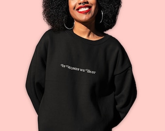 May include: Black sweatshirt with the text "In Women We Trust" embroidered in white on the front.