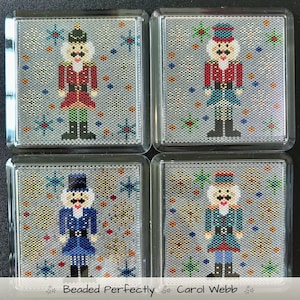 May include: Four square coasters with beaded nutcracker designs. Each coaster features a different nutcracker in red, blue, and green uniforms, set against a silver background with snowflake and star accents. The coasters are encased in clear plastic.