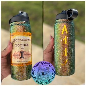 Puede incluir: Botella de agua brillante con tapa negra. Un lado presenta la etiqueta "Polyjuice Potion", el otro lado tiene el nombre "Ally" en amarillo. La botella tiene un diseño de purpurina verde y dorado.