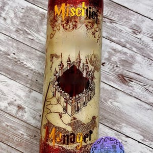 Puede incluir: Vaso rojo con purpurina con un diseño blanco y dorado que presenta un mapa de Hogwarts y el texto "Mischief Managed".