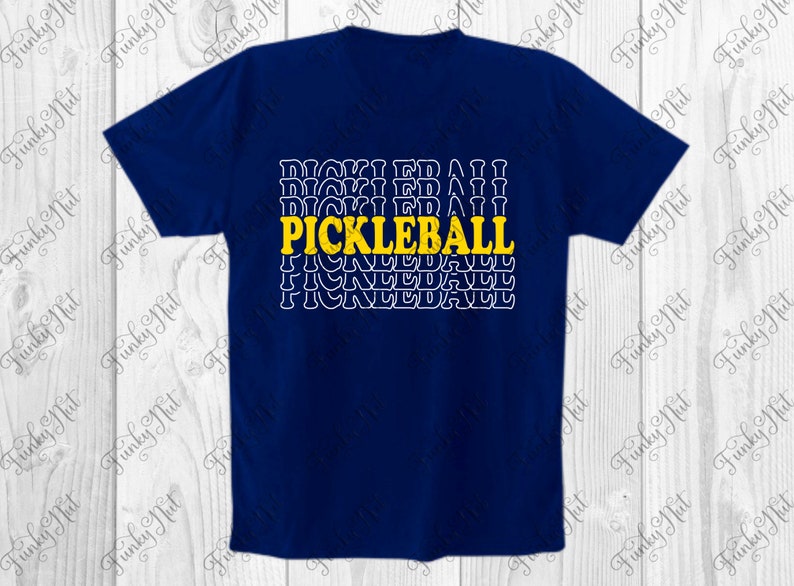 以下が含まれることがあります： ネイビーブルーのTシャツ。黄色で「PICKLEBALL」の文字がプリントされ、その下に白で繰り返される「PICKLEBALL」のデザイン。クルーネックのスタイルです。