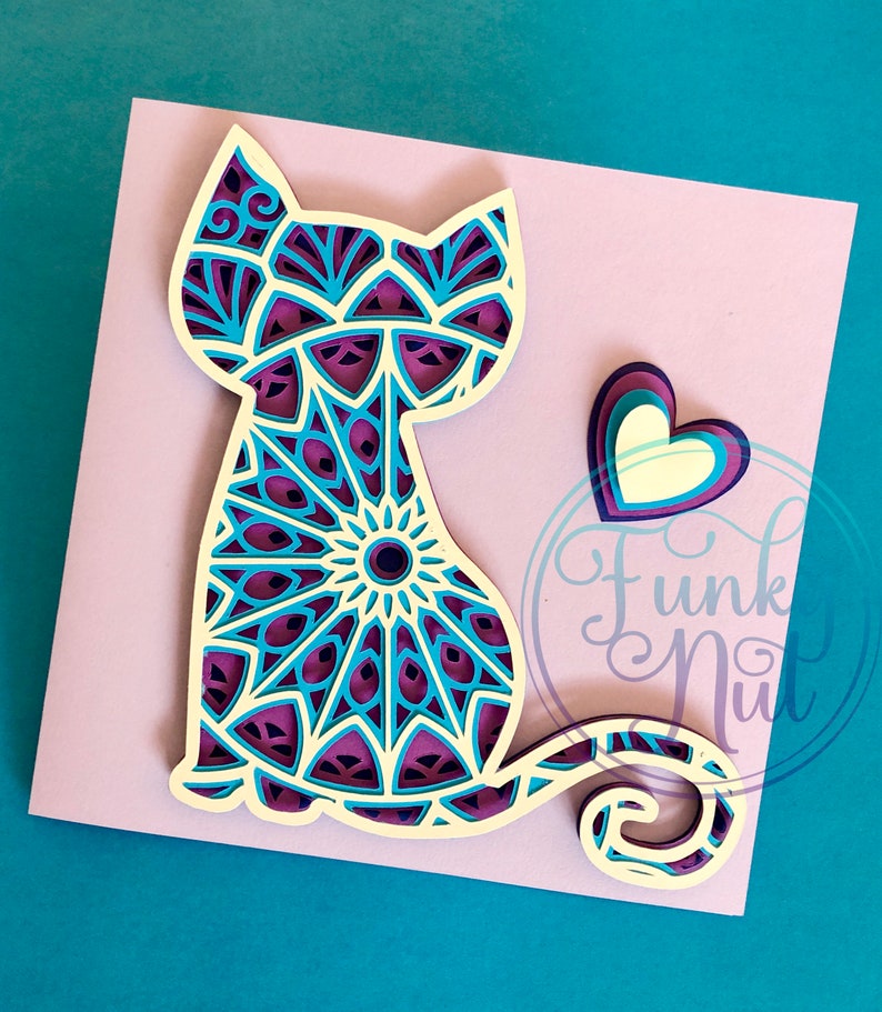 May include: A papercraft cat with a mandala design in shades of purple, blue, and white. The cat is sitting with its tail curled around its body. A layered heart in shades of purple and white is to the right of the cat.
