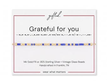 May include: A delicate bracelet featuring alternating small gold-tone beads and vibrant blue cylindrical glass beads, displayed on a white card with the text "gifted.", "Grateful for you", Morse code, and "14k Gold Fill or .925 Sterling Silver".