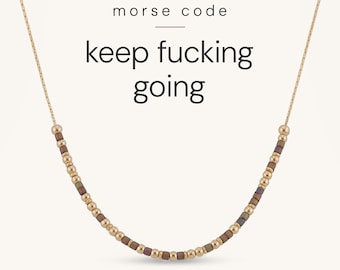 May include: A gold-toned chain necklace featuring a series of small, alternating metallic gold and dark-coloured beads arranged in a pattern. The text "morse code" and "keep fucking going" is displayed in black above the necklace.
