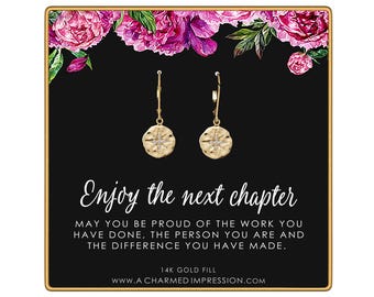 May include: A pair of gold-tone drop earrings with a starburst design on a black display card featuring pink floral accents and the text: Enjoy the next chapter. May you be proud of the work you have done, the person you are and the difference you have made. 14K gold fill.