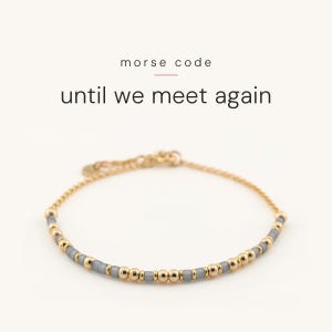 May include: A gold chain bracelet featuring a pattern of small metallic gold beads and matte grey cylindrical beads arranged in a Morse code sequence. The text above the bracelet reads morse code until we meet again in black font.