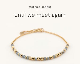 May include: A gold chain bracelet featuring a Morse code pattern made of small, round, metallic gold beads and cylindrical, translucent grey beads. The text "morse code" and "until we meet again" is printed above the bracelet.