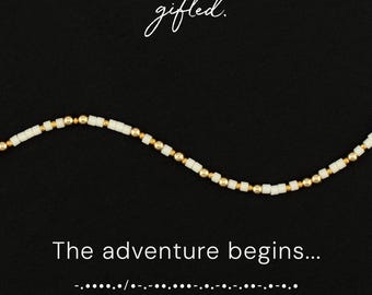 May include: A beaded bracelet featuring alternating white cylindrical beads and small metallic gold spherical beads. The image includes the text gifted. and The adventure begins... followed by a sequence of Morse code dots and dashes.