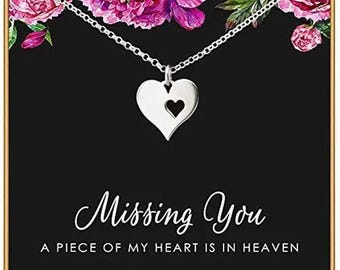 May include: A silver heart-shaped pendant necklace with a small heart cutout, displayed on a black card featuring pink floral accents and the text: Missing You, A PIECE OF MY HEART IS IN HEAVEN, STERLING SILVER, WWW.ACHARMEDIMPRESSION.COM.