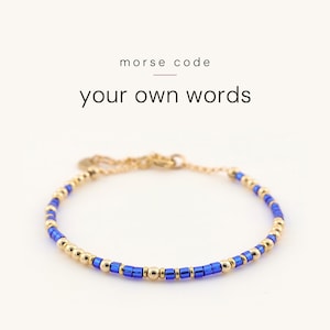 May include: A delicate bracelet featuring alternating metallic gold-tone beads and vibrant blue cylindrical beads arranged in a pattern. The text above the bracelet reads morse code your own words. The bracelet includes a thin gold-tone chain.