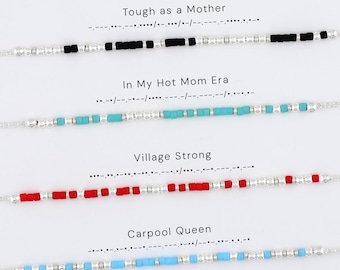 May include: Four beaded bracelets featuring Morse code patterns. The first has black beads, the second turquoise, the third red, and the fourth light blue, all interspersed with silver-toned metallic beads. Each bracelet is labeled with text.