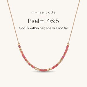 May include: A delicate gold chain necklace featuring a Morse code pattern made of small metallic gold and pink cylindrical beads. The text above the necklace reads: morse code, Psalm 46:5, God is within her, she will not fall.