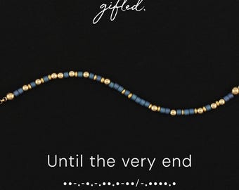 May include: A beaded bracelet featuring alternating matte slate blue cylindrical beads and metallic gold spherical beads. The text gifted. appears above the bracelet, while the text Until the very end and Morse code are printed below the jewelry.