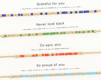 May include: Four beaded bracelets featuring gold-tone spacers and colored beads arranged in Morse code patterns. The bracelets include the phrases Grateful for you, Never look back, Do epic shit, and So proud of you printed above each corresponding design.