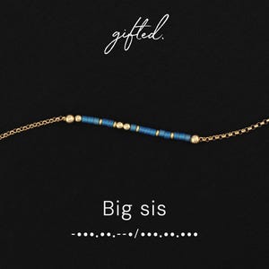 May include: A gold-colored chain necklace with a series of blue and gold beads. The necklace has the text "Big sis" below it, and the word "gifted" in cursive at the top. The background is black.