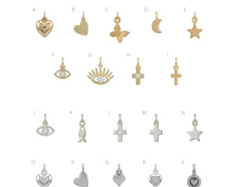 May include: A collection of nineteen gold and silver metal charms labeled A through S. The charms feature various shapes including hearts, a butterfly, a crescent moon, stars, evil eyes with clear stones, crosses, a fish, and circular designs.