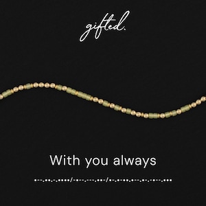 Könnte beinhalten: Eine Perlenkette mit abwechselnden matten, salbeigrünen zylindrischen Perlen und kleinen metallisch goldenen runden Perlen. Der Text gifted. steht oben, während der Text With you always und Morsezeichen-Punkte und -Striche unten zu sehen sind.