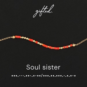 May include: A delicate bracelet featuring a sequence of small, cylindrical coral-colored beads and round gold-toned metallic beads. The text gifted. appears above the bracelet, while Soul sister and Morse code dots and dashes appear below.