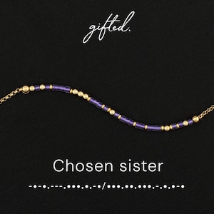 May include: A delicate bracelet featuring alternating purple cylindrical beads and small gold-toned spherical beads on a thin chain. The text "gifted." appears at the top, with "Chosen sister" and Morse code dots and dashes at the bottom.