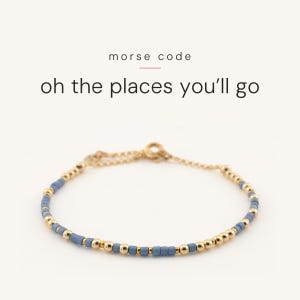 May include: A delicate bracelet featuring alternating light blue cylindrical beads and small gold-toned spherical beads. The text "morse code" and "oh the places you'll go" is printed above the bracelet, which includes a gold-toned chain and clasp.