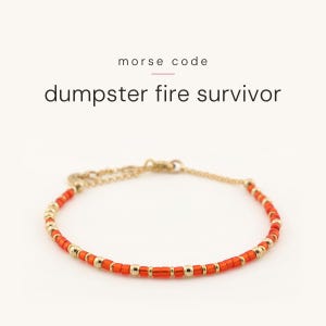 May include: A bracelet featuring orange and gold-toned beads arranged in a pattern representing Morse code. The text above the bracelet reads morse code dumpster fire survivor. The bracelet includes a gold-toned chain and a lobster claw clasp.