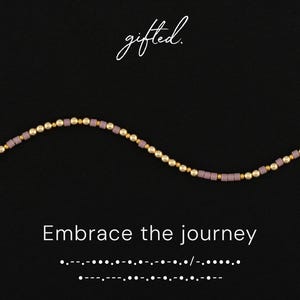 May include: A necklace with a wavy design, featuring small gold beads and lavender-colored square beads. The phrase "Embrace the journey" is displayed in white text on a black background, along with the word "gifted" in cursive.