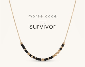 May include: A gold chain necklace featuring a series of black and gold beads arranged in a Morse code pattern. The text "morse code" and "survivor" is printed above the necklace. The beads alternate between small black cylinders and gold spheres.