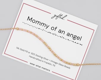 May include: A delicate bracelet featuring alternating light pink glass beads and small gold-toned metallic beads, displayed on a white card with the text "gifted.", "Mommy of an angel", Morse code, and "14k Gold Fill or .925 Sterling Silver".