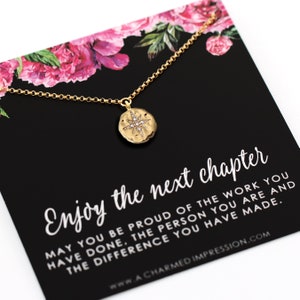 May include: A gold-tone necklace with a circular pendant featuring a starburst design and small clear stones. The necklace is displayed on a black card with pink floral accents and the text: Enjoy the next chapter. May you be proud of the work you have done, the person you are and the difference you have made.
