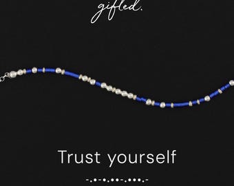 May include: A beaded bracelet featuring alternating metallic silver-toned spheres and vibrant blue cylindrical beads. The text gifted. appears at the top, while the phrase Trust yourself and Morse code dots and dashes are printed below.