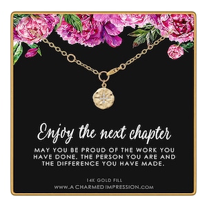 May include: A gold-colored necklace with a circular pendant featuring a starburst design and small crystals. The necklace is displayed on a black background with the text "Enjoy the next chapter". Pink and purple flowers are at the top.