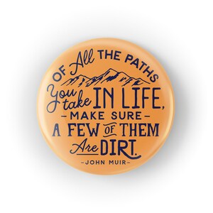 May include: Orange round button with a quote about life and mountains. The quote reads "Of all the paths you take in life, make sure a few of them are dirt." - John Muir.