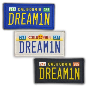 May include: Three different versions of a California license plate patch with the text "DREAM1N" in yellow letters on a blue, white, and black background. The license plate numbers are 247 and 365.