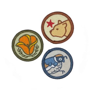 May include: Three embroidered patches with a California theme. The first patch is green and features a yellow California poppy flower. The second patch is brown and features a tan bear with a red star. The third patch is blue and features a blue and white bird.